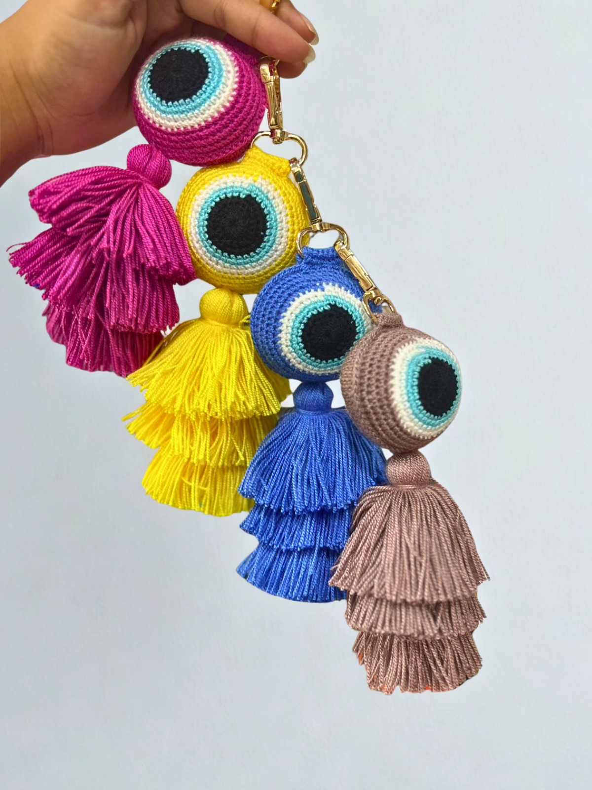 Colorful tassel keychains with eye design held by a hand against a light gray background