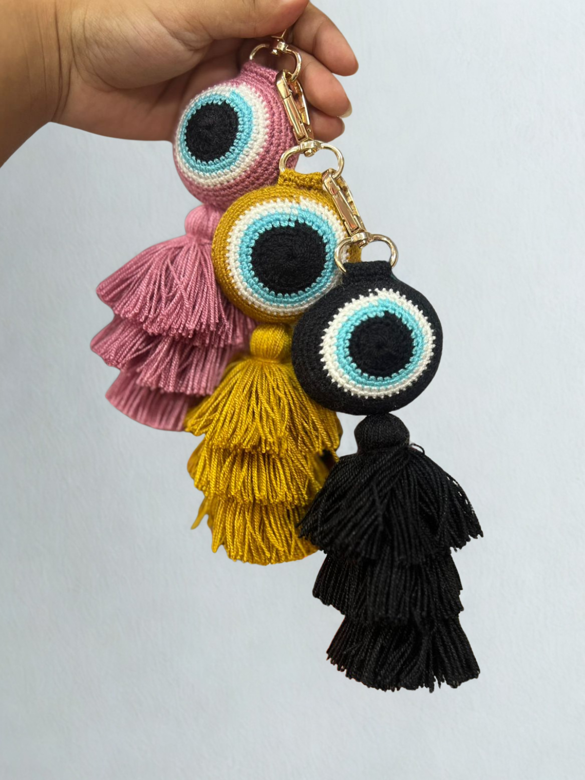 Colorful tassel keychain with eye design held by a hand against a light gray background