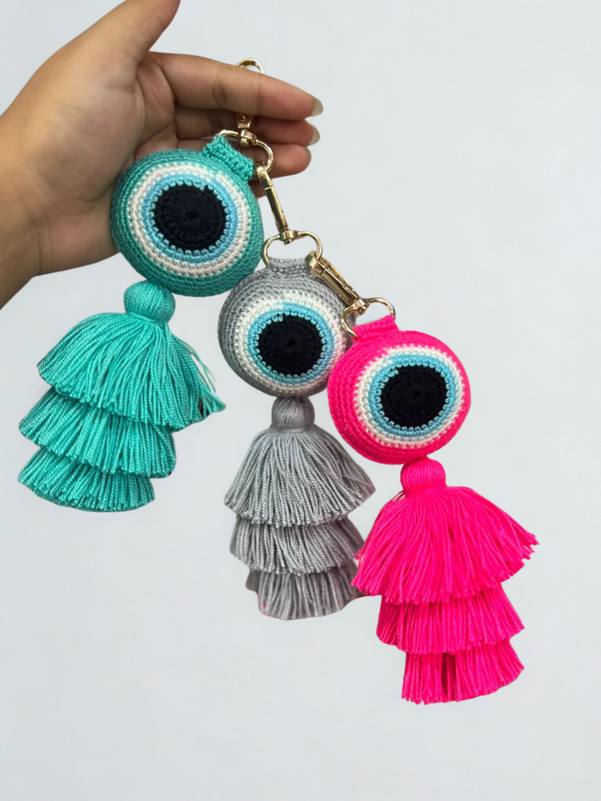 Three colorful tassel keychains held by a hand against a white background