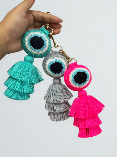 Three colorful tassel keychains held by a hand against a white background