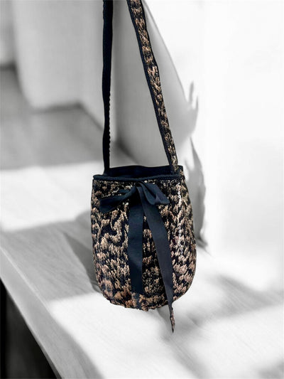 Leopard print handbag with a black ribbon on a light wooden surface