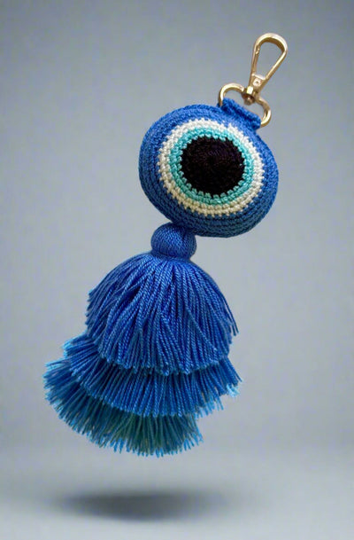 Blue tassel keychain with evil eye design on a light gray background