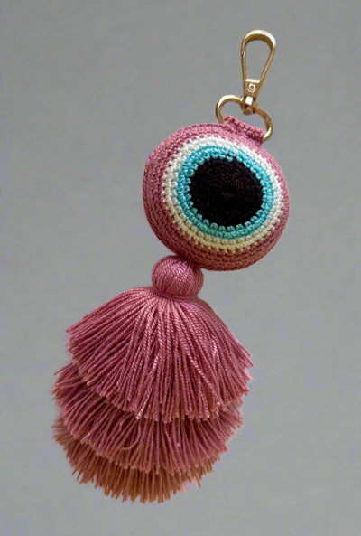 Pink tassel keychain with multicolored eye design on a light gray background