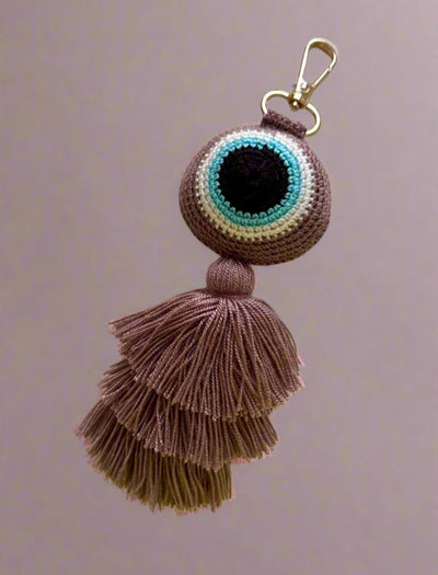 Crocheted keychain with tassels and eye design on a light gray background