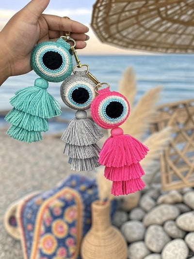 Three colorful tassel keychains held by a hand with a beach background.