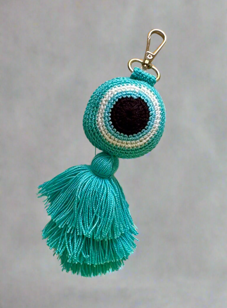 Turquoise evil eye keychain with tassel on a gray background