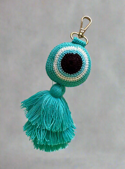 Turquoise evil eye keychain with tassel on a gray background